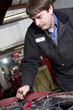 Photo: Automotive Technician Works Under the Car Hood in Auto Repair Automotive Technician Works Under the Car Hood in Auto Repair