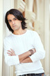 Dark-haired man with folded hands stands leaning to wall