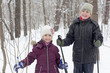Smiling boy and his younger sister stand in winter park with ski