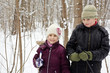 Boy and his younger sister stand in winter park with ski poles