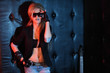Young woman rocker in big sunglasses stands near wall