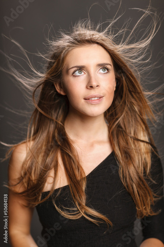 Photo: Portrait of young woman with hair flying, over gray background Portrait of young woman with hair flying, over gray background