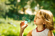Funny little girl blowing soap bubbles outdoor