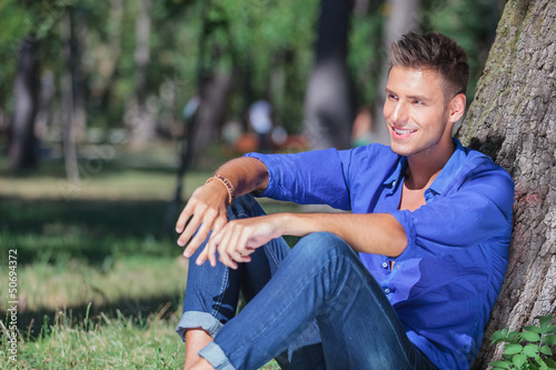 Photo: seated man leaning on tree looks away seated man leaning on tree looks away