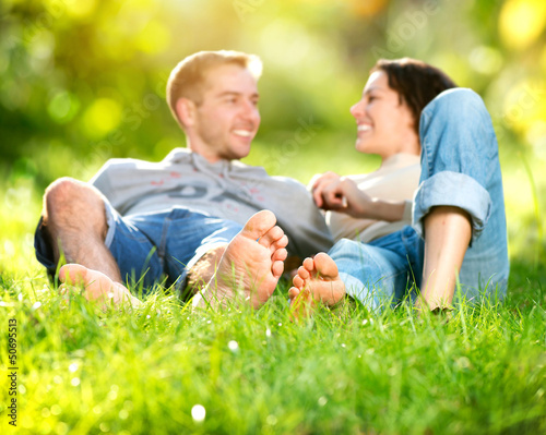 Photo: Park. Young Couple Lying on Grass Outdoor Park. Young Couple Lying on Grass Outdoor