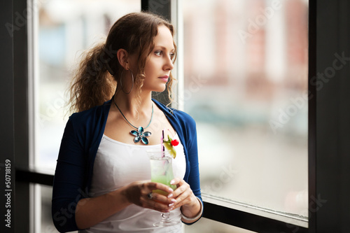 Photo: Sad woman with coctail looking out the window Sad woman with coctail looking out the window