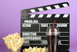 Movie clapperboard, cola and popcorn on purple background