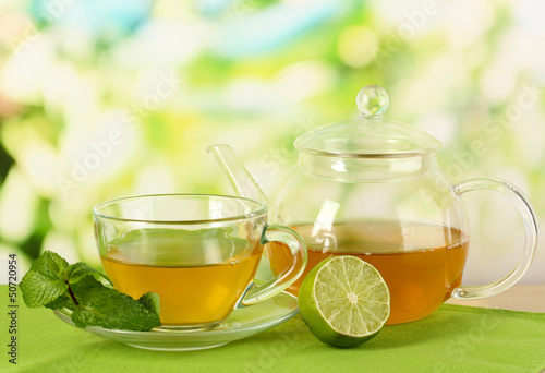 Photo: Cup of tea with mint and lime on table on bright background Cup of tea with mint and lime on table on bright background