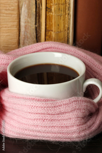 Photo: Cup of coffee wrapped in scarf on books background Cup of coffee wrapped in scarf on books background