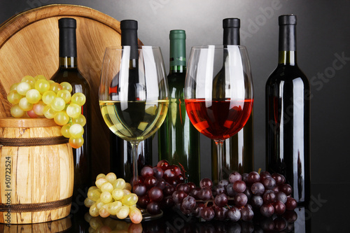 Photo: Assortment of wine in glasses and bottles on grey background Assortment of wine in glasses and bottles on grey background