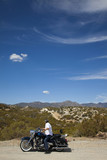 Photo: Senior man riding motorcycle on desert road looking to mountains in background Senior man riding motorcycle on desert road looking to mountains in background