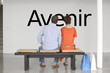 Photo: Rear view of couple seated on bench reading French text "Avenir" (future) on wall Rear view of couple seated on bench reading French text "Avenir" (future) on wall