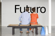 Photo: Rear view of couple seated on bench reading Spanish text "Futuro" (future) on wall Rear view of couple seated on bench reading Spanish text "Futuro" (future) on wall
