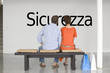 Photo: Rear view of couple reading Italian text "Sicurezza" (security) and contemplating about future security Rear view of couple reading Italian text "Sicurezza" (security) and contemplating about future security