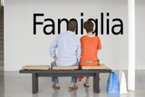 Photo: Rear view of couple seated on bench reading Italian text "Famiglia" (family) on wall Rear view of couple seated on bench reading Italian text "Famiglia" (family) on wall