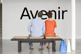 Photo: Rear view of couple seated on bench reading French text "Avenir" (future) on wall Rear view of couple seated on bench reading French text "Avenir" (future) on wall