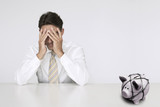 Photo: Worried businessman at table with trapped piggy bank representing financial difficulties Worried businessman at table with trapped piggy bank representing financial difficulties