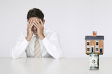 Photo: Worried businessman at table with house on top of bills representing increasing real estate rates Worried businessman at table with house on top of bills representing increasing real estate rates