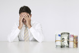 Photo: Worried businessman at table with money rolls representing financial problems Worried businessman at table with money rolls representing financial problems