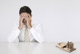 Photo: Worried businessman at table model home in mouse trap representing expensive real estate costs Worried businessman at table model home in mouse trap representing expensive real estate costs