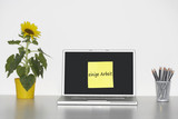 Photo: Sunflower plant on desk and sticky notepaper on laptop screen with "einige Arbeit" written on it in German Sunflower plant on desk and sticky notepaper on laptop screen with "einige Arbeit" written on it in German