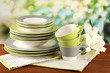 Empty plates and cups on wooden table on green background