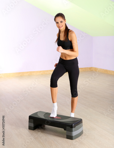 Photo: Young woman doing fitness exercises on stepper at gymnasium Young woman doing fitness exercises on stepper at gymnasium