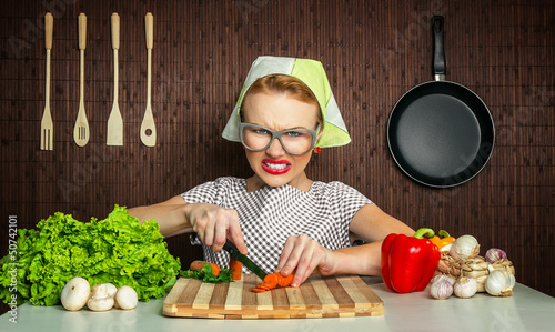 Photo: Happy funny woman cook working in the kitchen cutting carrot Happy funny woman cook working in the kitchen cutting carrot