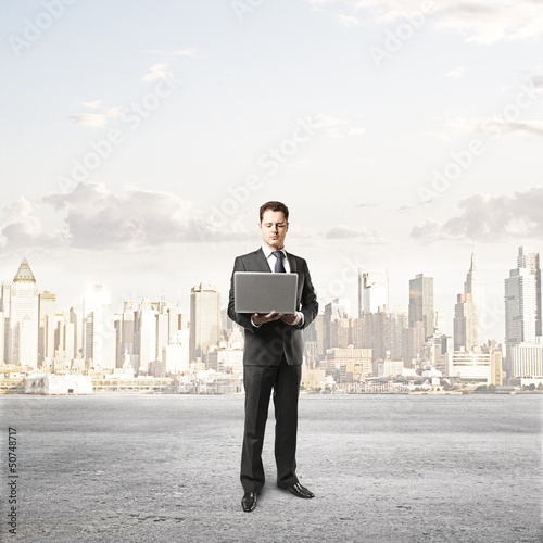 Photo: businessman with laptop and city on background businessman with laptop and city on background