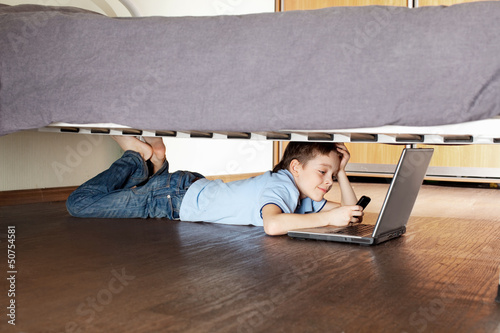 Photo: Child with laptop and phone under the bed Child with laptop and phone under the bed