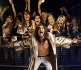 Photo: Portrait of young man in fur coat screaming with excited audience in the background Portrait of young man in fur coat screaming with excited audience in the background