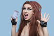 Photo: Portrait of funky young woman screaming while using cell phone over blue background Portrait of funky young woman screaming while using cell phone over blue background