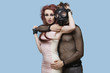 Photo: Portrait of young man wearing gas mask embraces funky woman over blue background Portrait of young man wearing gas mask embraces funky woman over blue background