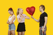 Photo: Young man gifting heart shaped balloon to surprised woman with friend feeling left out standing behind Young man gifting heart shaped balloon to surprised woman with friend feeling left out standing behind
