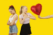 Photo: Man's hand gifting heart shaped balloon to surprised woman with friend feeling left out standing behind Man's hand gifting heart shaped balloon to surprised woman with friend feeling left out standing behind