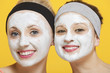 Photo: Portrait of two happy women with face pack on their faces over yellow background Portrait of two happy women with face pack on their faces over yellow background