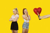 Photo: Man's hand gifting heart shaped balloon and champagne bottle to surprised woman with friend feeling left out standing behind Man's hand gifting heart shaped balloon and champagne bottle to surprised woman with friend feeling left out standing behind