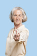 Foto: Portrait of senior woman in casuals making rebellious gesture against blue background Portrait of senior woman in casuals making rebellious gesture against blue background