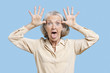 Foto: Portrait of senior woman making funny faces with hands on head against blue background Portrait of senior woman making funny faces with hands on head against blue background
