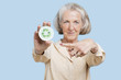 Photo: Portrait of senior woman holding badge with recycling symbol against blue background Portrait of senior woman holding badge with recycling symbol against blue background