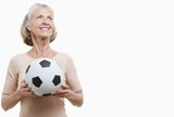 Photo: Smiling senior woman in casuals holding soccer ball against white background Smiling senior woman in casuals holding soccer ball against white background