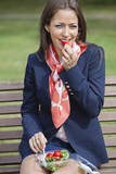 Photo: Portrait of a young businesswoman eating salad while sitting on bench at park Portrait of a young businesswoman eating salad while sitting on bench at park