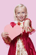 Foto: Portrait of a happy young girl dressed in princess costume holding paper heart as she displays ring over pink background Portrait of a happy young girl dressed in princess costume holding paper heart as she displays ring over pink background