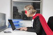 Photo: Side view of senior businesswoman in superhero costume using laptop at office desk Side view of senior businesswoman in superhero costume using laptop at office desk