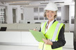 Photo: Portrait of smiling senior woman in reflector vest and hard hat holding clipboard at office Portrait of smiling senior woman in reflector vest and hard hat holding clipboard at office
