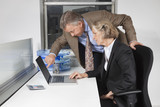 Photo: Side view of businesswoman and man looking at laptop screen at desk in office Side view of businesswoman and man looking at laptop screen at desk in office