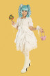 Photo: Full length portrait of young woman dressed as a doll holding lollipop over yellow background Full length portrait of young woman dressed as a doll holding lollipop over yellow background