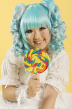 Photo: Portrait of smiling young woman dressed as a doll holding lollipop over yellow background Portrait of smiling young woman dressed as a doll holding lollipop over yellow background