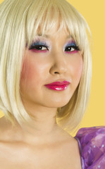 Photo: Portrait of young woman with blond hair and eyeshadow smiling against yellow background Portrait of young woman with blond hair and eyeshadow smiling against yellow background