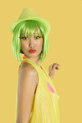 Photo: Portrait of funky young woman with green hair puckering her lips against yellow background Portrait of funky young woman with green hair puckering her lips against yellow background